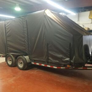 Large trailer covered with a black tarp parked indoors.