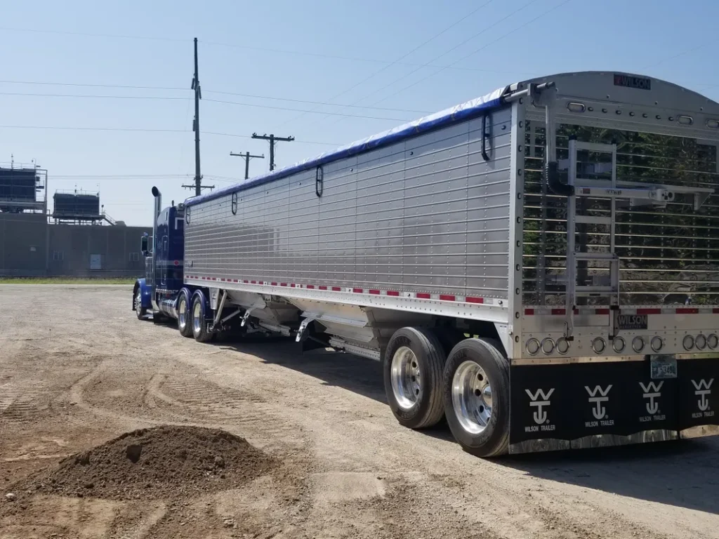 Blue semi-truck with a large silver trailer parked on dirt ground.