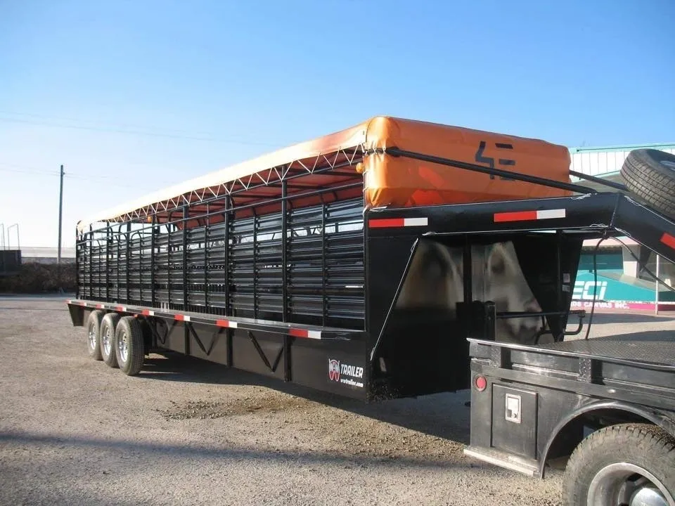 A large livestock trailer attached to a black truck under a clear sky.