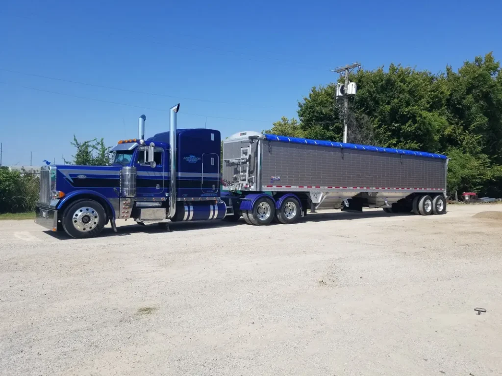 A large blue semi-truck parked on a dirt road under clear skies.