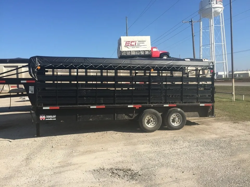 Black livestock trailer parked on gravel with a truck in the background.