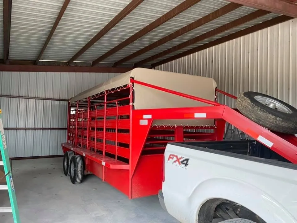 Red livestock trailer hitched to a white truck inside a barn.