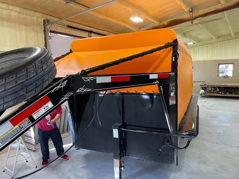 Black trailer with an orange tarp cover inside a building.