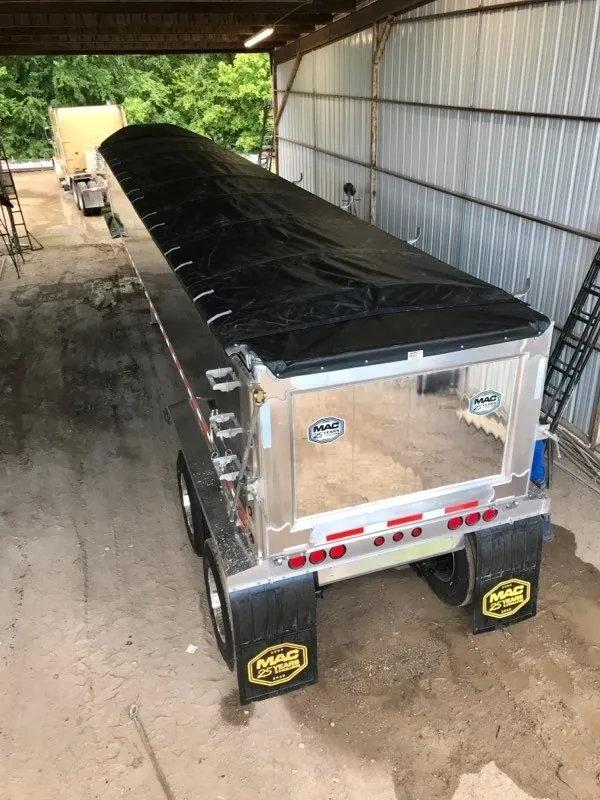 A shiny aluminum dump trailer with a black tarp cover in a garage.