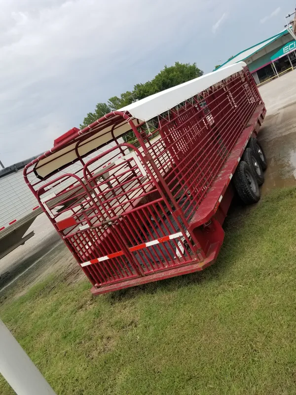 Red livestock trailer parked on grass near water.