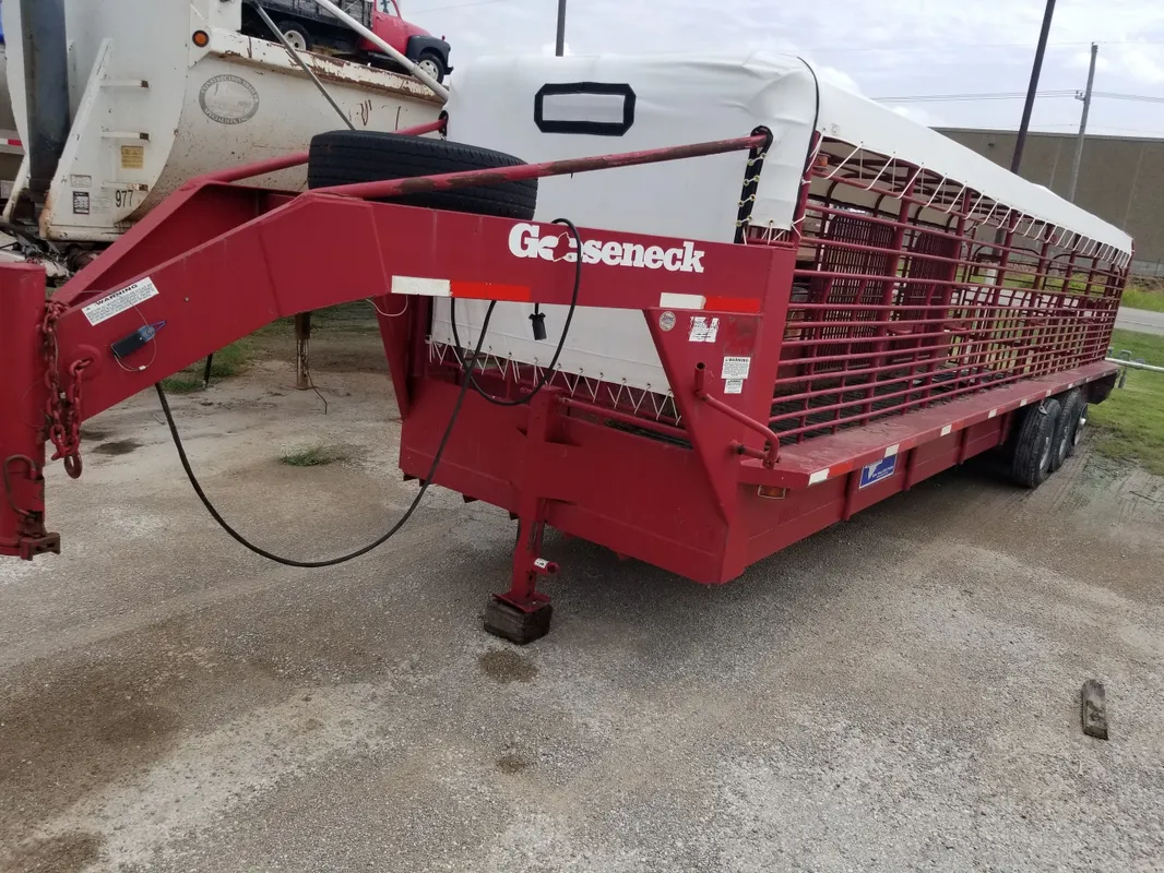 Red Gooseneck livestock trailer parked on concrete.